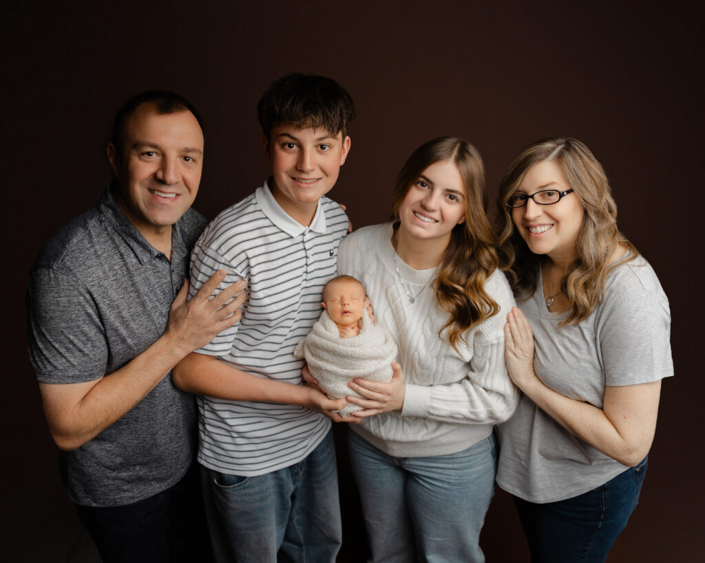 Family newborn portrait showing parents and siblings gathered around their baby in a coordinated, neutral color palette