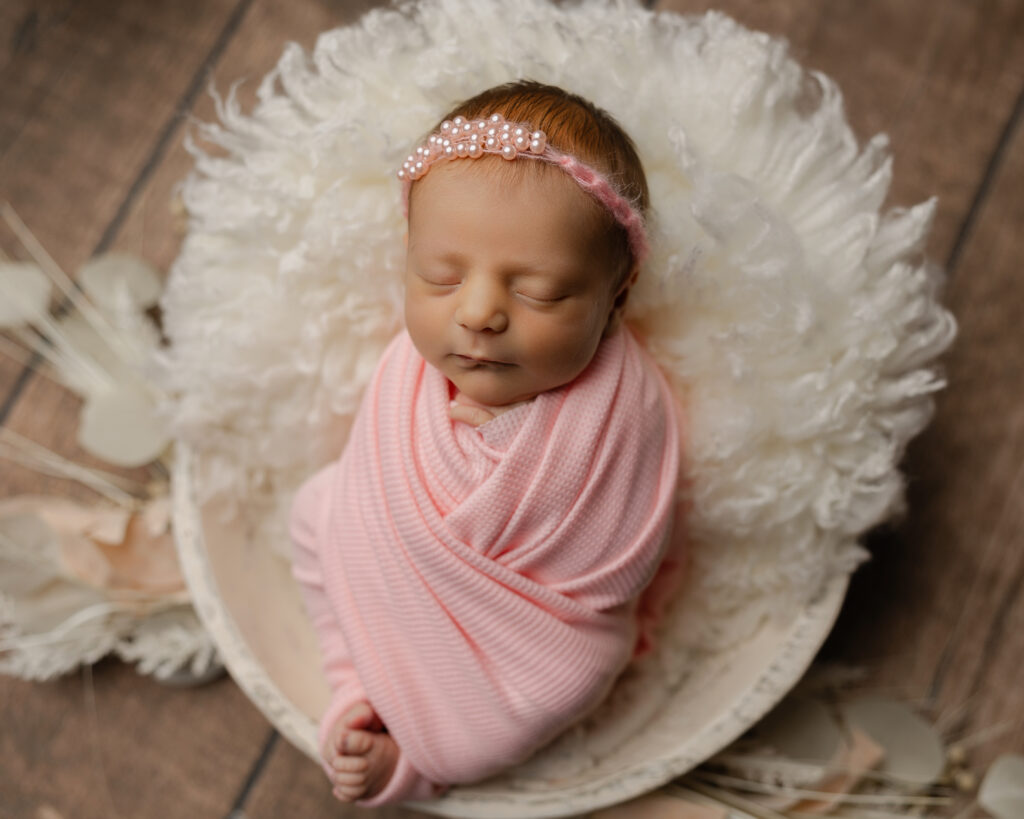 Simple newborn photo outfit ideas using a pink swaddle and delicate headband for a timeless studio portrait