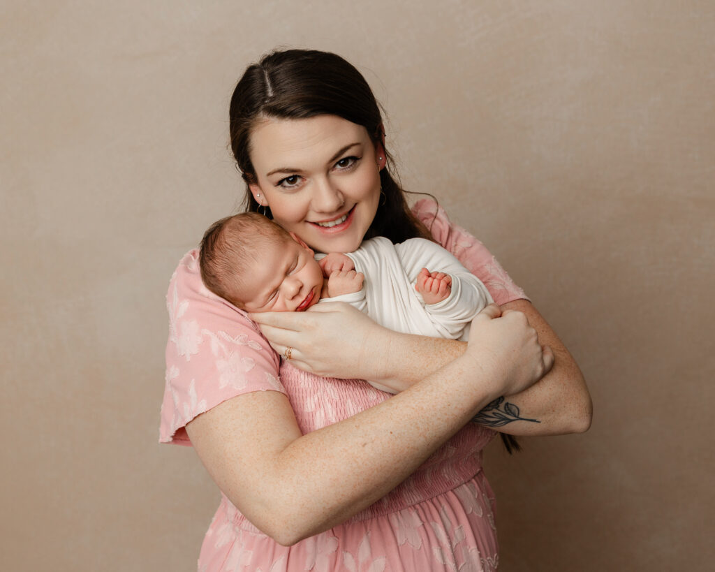 Mother cuddling her sleeping newborn close in a soft pink dress. Photograph by Kaitlyn Dawn Photography.