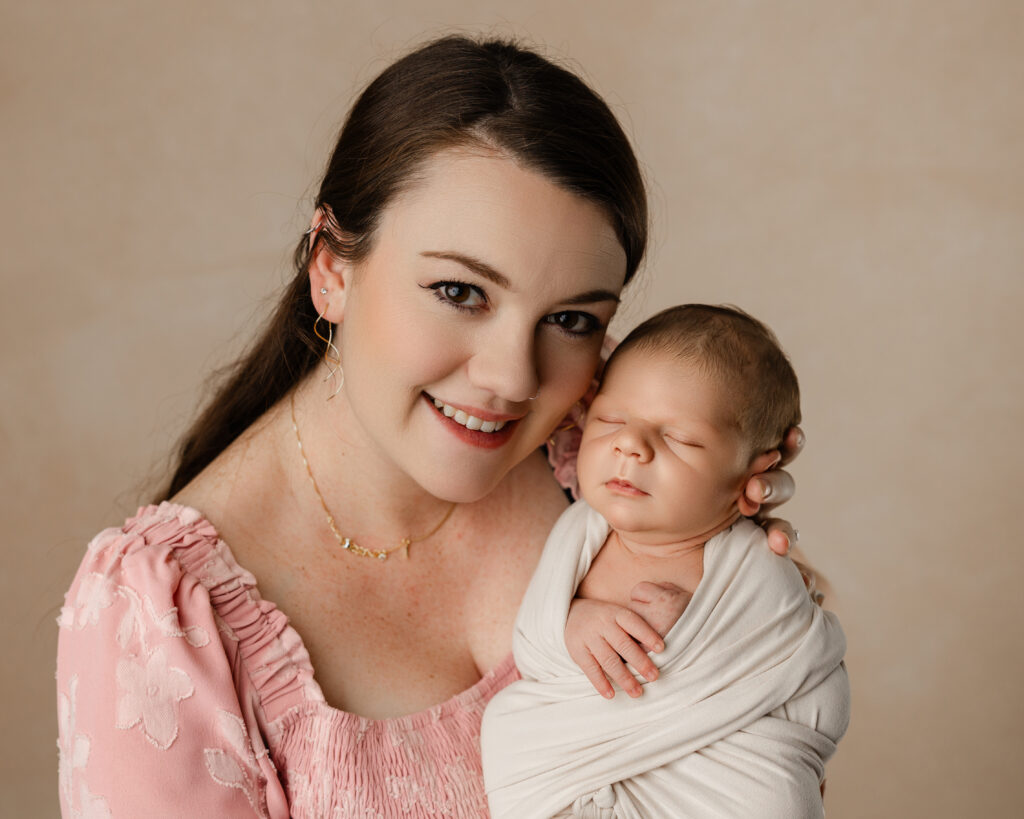 Mother smiling while holding her wrapped newborn during a studio session showing how motherhood changes you. Photograph by Kaitlyn Dawn Photography.