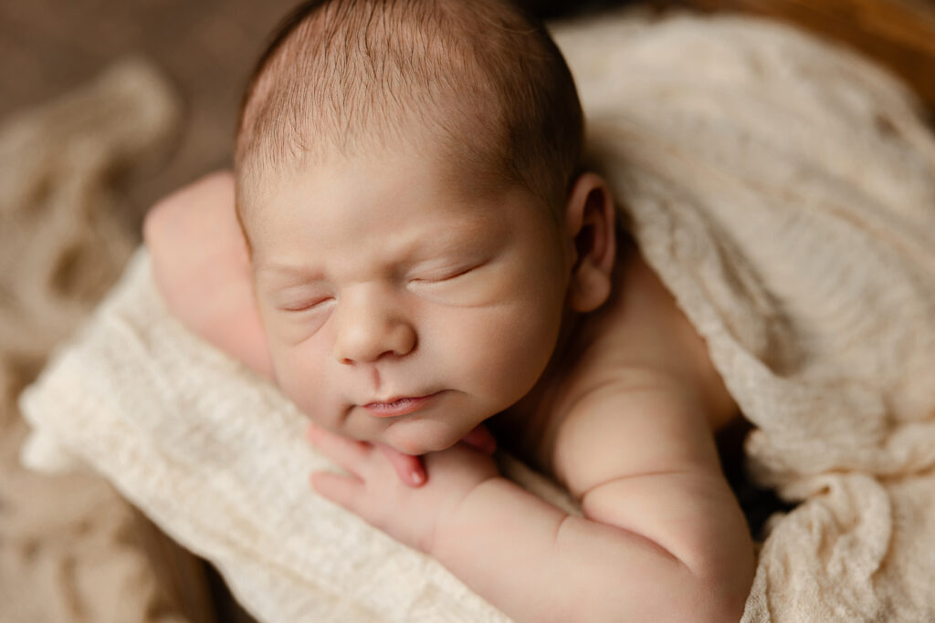 Newborn baby sleeping peacefully while swaddled in a cream blanket. Photograph by Redlands newborn photographer Kaitlyn Dawn Photography.