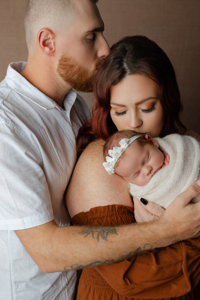 Parents gently holding their newborn during a Beaumont newborn and family photography session, captured in warm studio light.