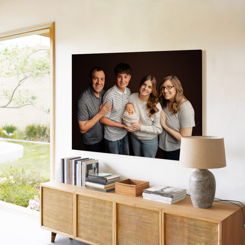 A modern family of five smiles together in a studio portrait displayed as a large wall art piece above a sleek wood cabinet. The framed artwork becomes the warm, joyful centerpiece of their home. Captured by Inland Empire portrait photographer Kaitlyn Dawn Photography.