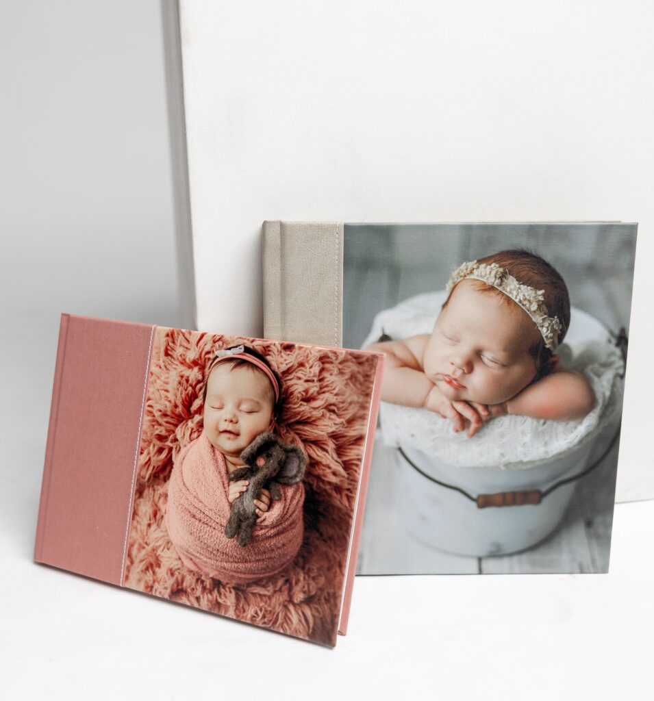 Two premium heirloom photo albums are displayed one in rose linen and another in a textured canvas cover each showcasing a newborn image on the front. These keepsakes are made to preserve your family’s most treasured moments. Products by Kaitlyn Dawn Photography, Inland Empire newborn photographer.