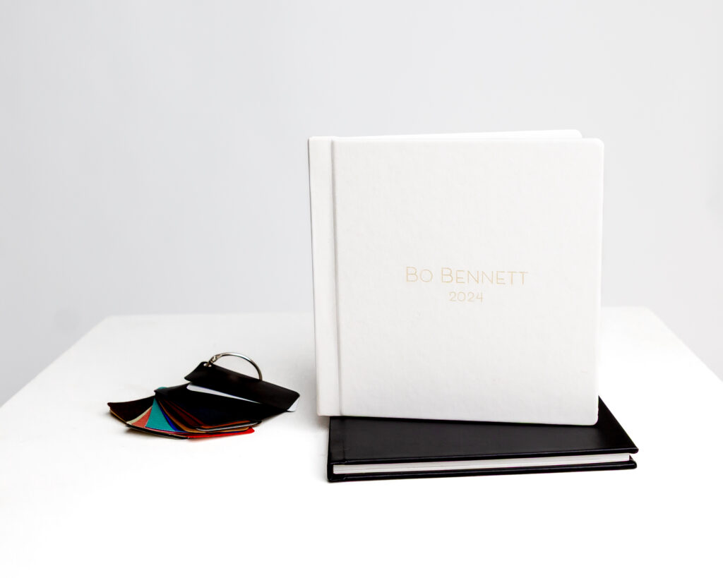 Custom white heirloom album with gold foil stamping reading “Bo Bennett 2024,” displayed upright on top of a black album with a color swatch ring beside them on a clean white table.
Photographed by Inland Empire photographer Kaitlyn Dawn Photography.