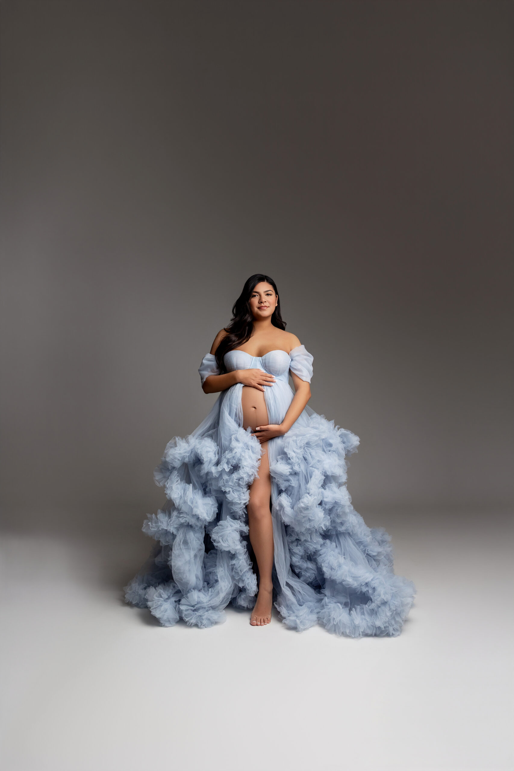 Soft blue couture maternity gown with flowing ruffled details photographed in a studio setting, featuring elegant maternity clothes in the Inland Empire for timeless and luxurious maternity portraits by Kaitlyn Dawn Photography.