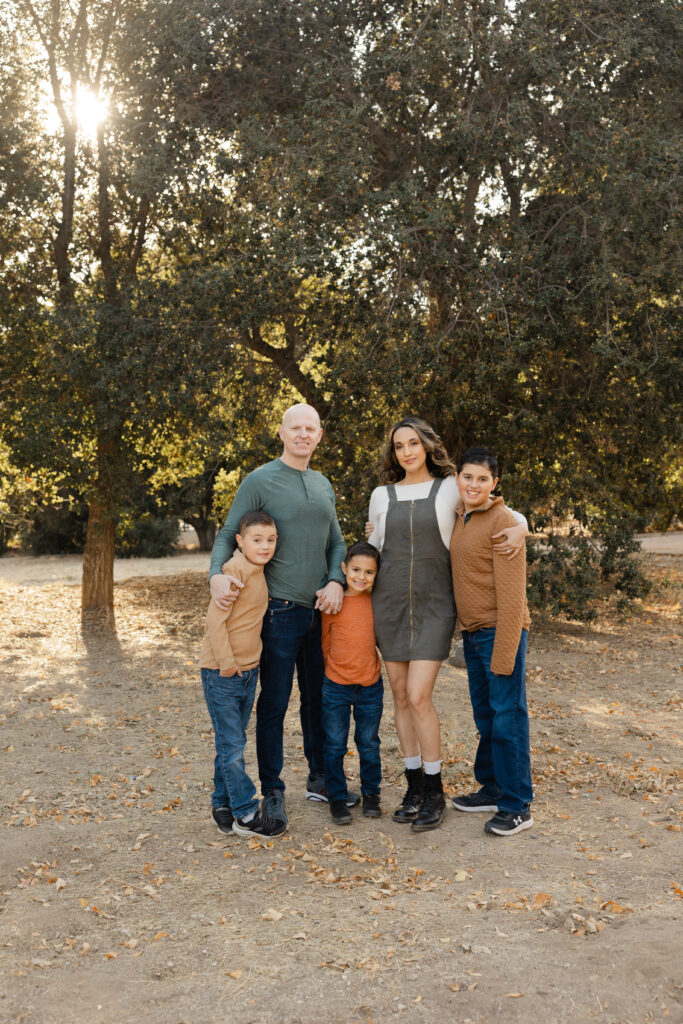 Family of five standing together outdoors during a Beaumont family photography session, surrounded by fall leaves and trees.