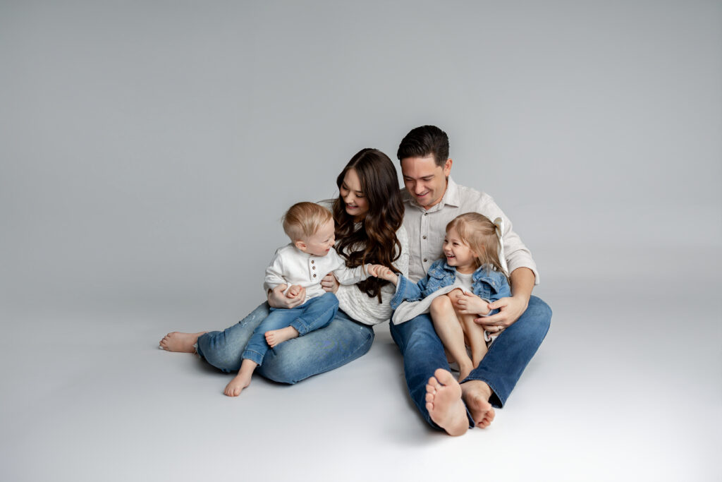 Family of four sitting together on a studio floor during a Beaumont family photography session, sharing playful and natural moments.