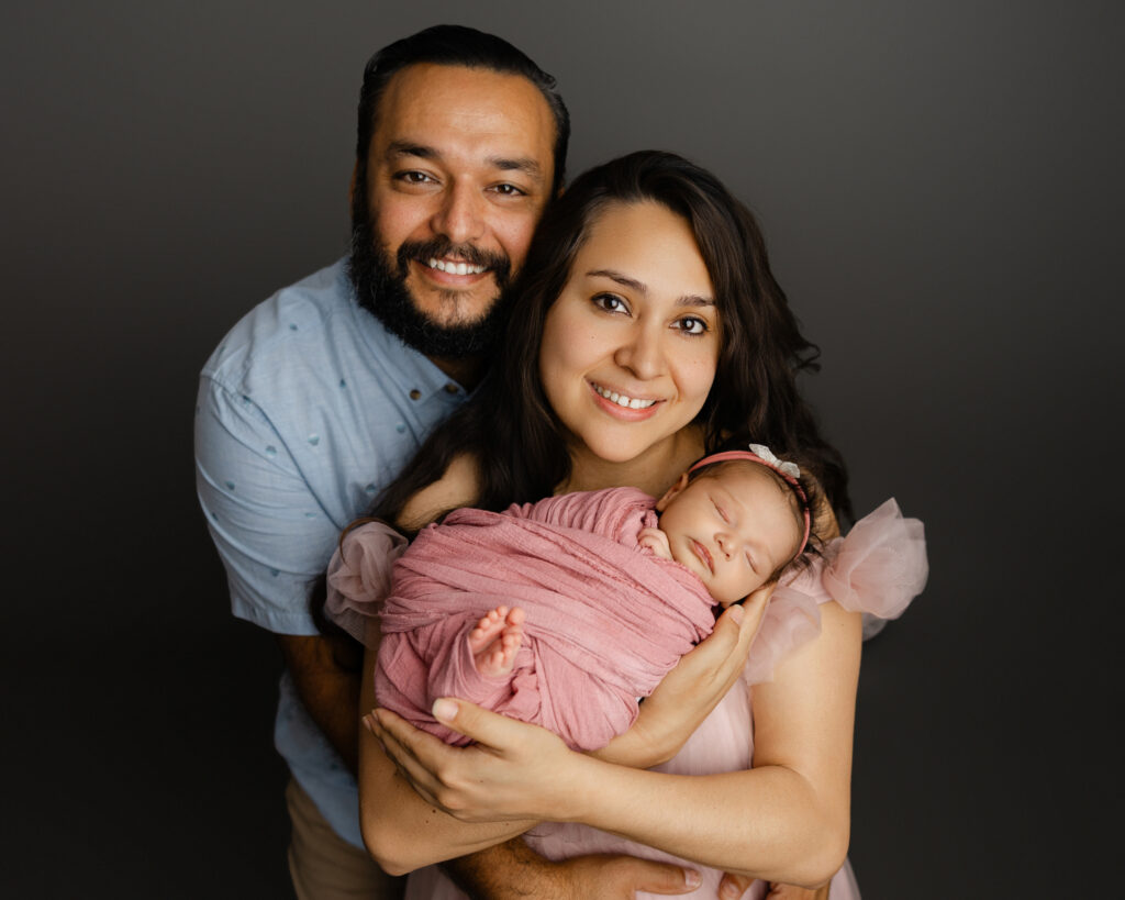 Smiling parents holding their newborn baby during a Redlands newborn photography session, captured in a simple studio setting