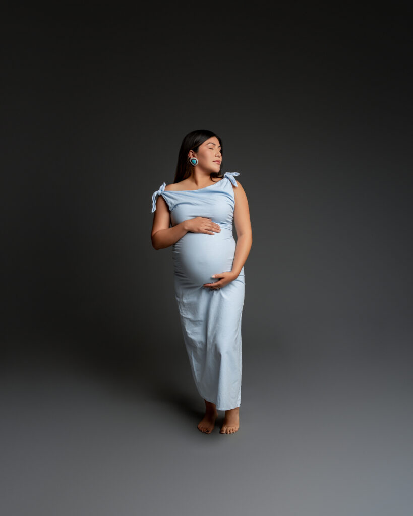 Studio maternity session featuring an expectant mother in a soft blue dress, photographed in the Inland Empire with a minimalist backdrop by Kaitlyn Dawn Photography