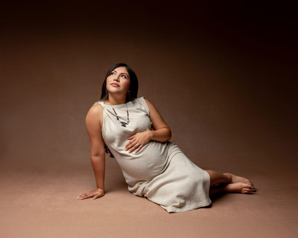 Elegant maternity photography session showing an expecting mother reclining on the studio floor in a neutral dress with Kaitlyn Dawn Photography