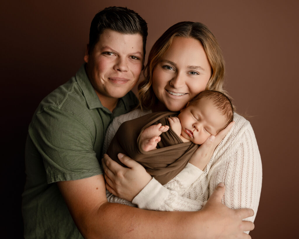 Family portrait from a Beaumont newborn photography session showing parents smiling while holding their peacefully sleeping newborn by Kaitlyn Dawn Photography