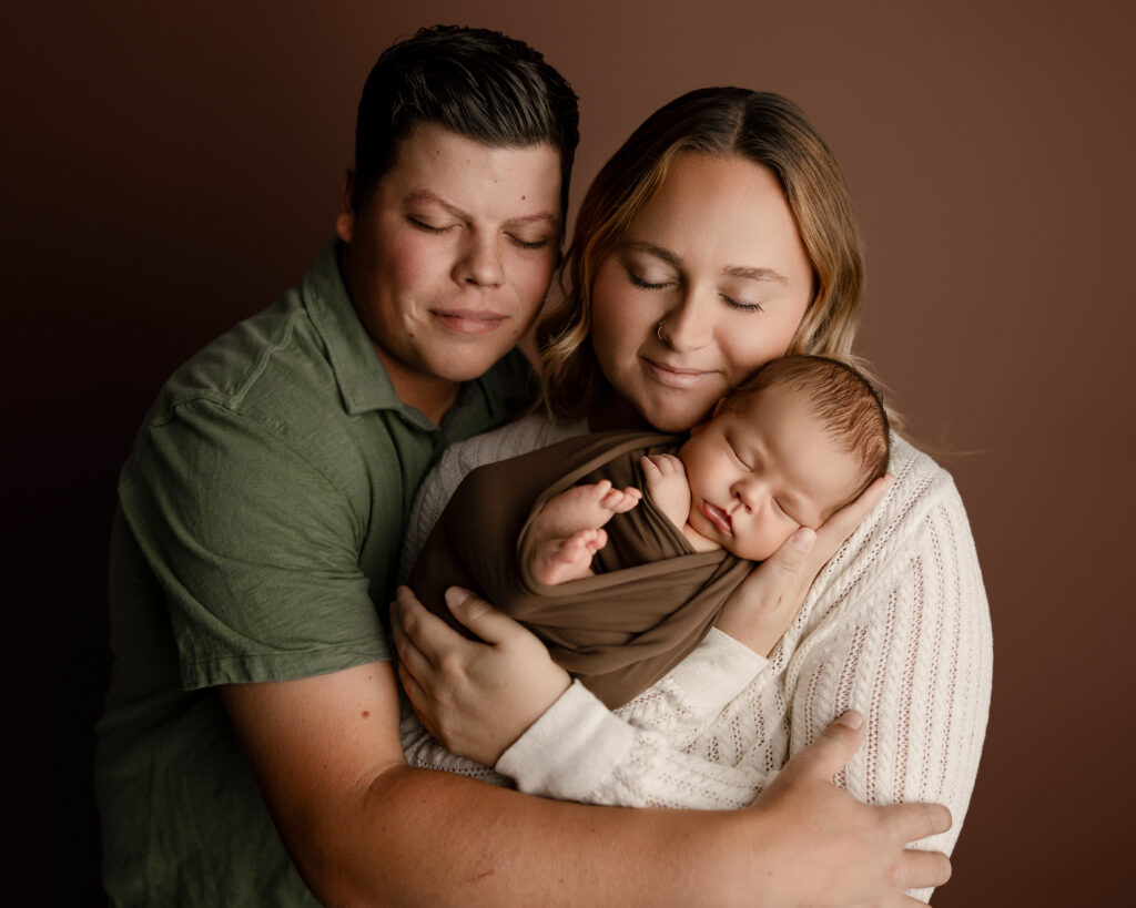 Beaumont newborn photography session featuring parents gently holding their swaddled newborn baby in a warm, neutral studio setting at Kaitlyn Dawn Photography