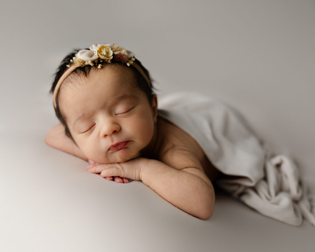 Newborn baby resting on a soft cream backdrop with a floral headband and light blanket. Photograph by Inland Empire newborn photographer Kaitlyn Dawn Photography.