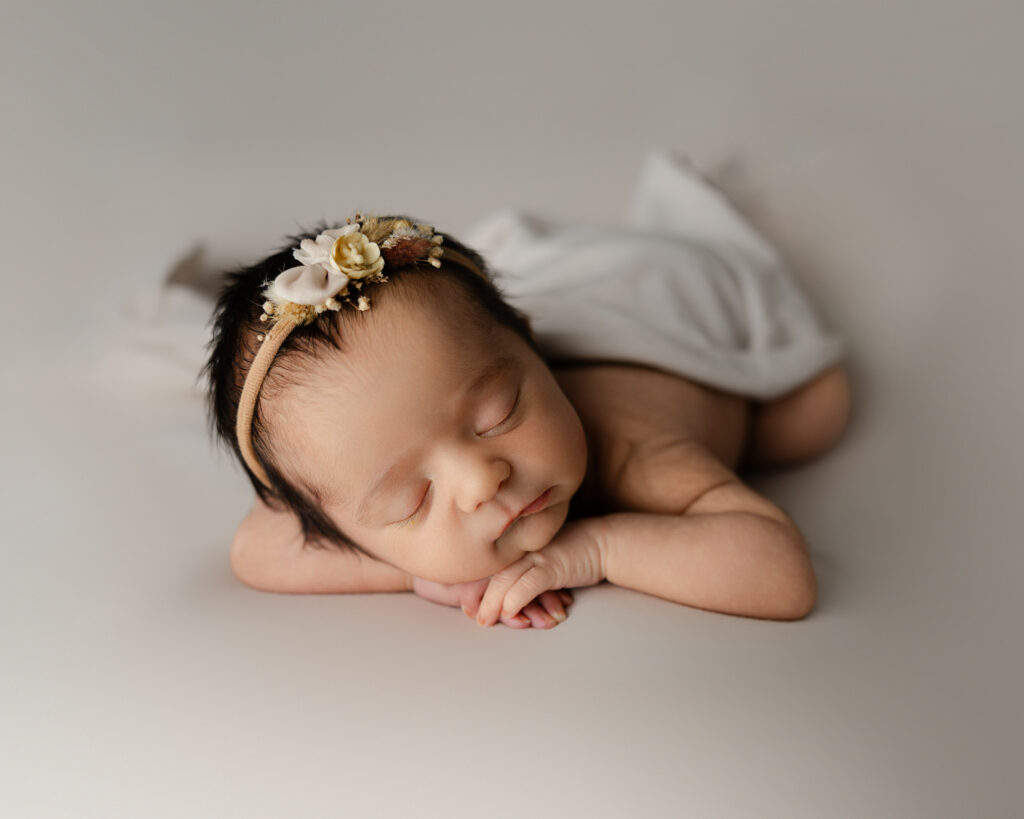 Sleeping newborn posed on a neutral backdrop with a delicate floral headband, representing the comfort and reassurance that new mom support can provide after birth.