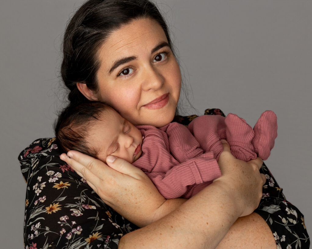 Mother kissing her newborn’s head against a soft gray backdrop, capturing how motherhood changes you. Photograph by Kaitlyn Dawn Photography.