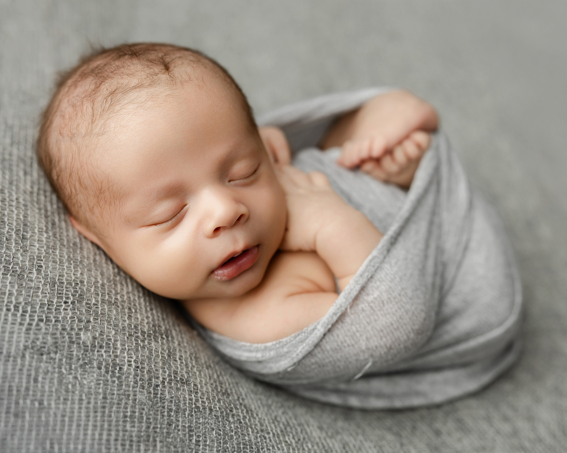 Sleeping newborn swaddled in a soft gray wrap, illustrating the peaceful rest parents hope for when researching a sleeping position for colic baby. Photograph by Inland Empire newborn photographer Kaitlyn Dawn Photography.