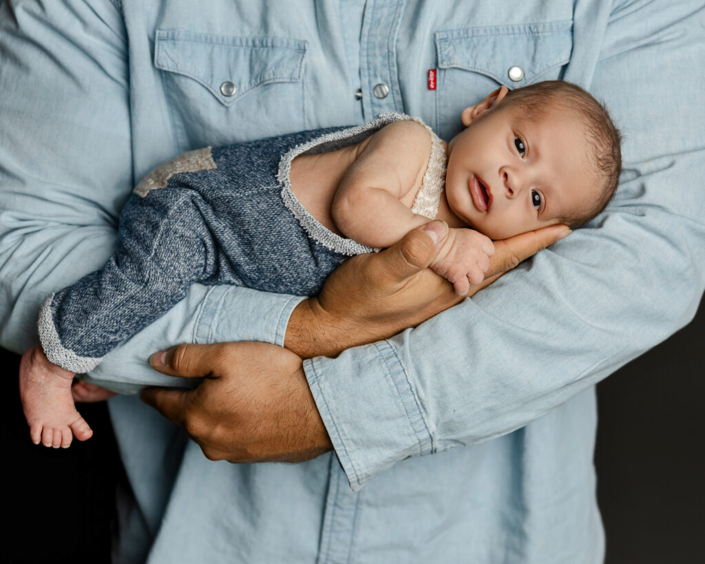 Father holding his newborn in a soothing cradle position often used to comfort infants while parents learn about a sleeping position for colic baby. Photograph by Redlands newborn photographer Kaitlyn Dawn Photography.