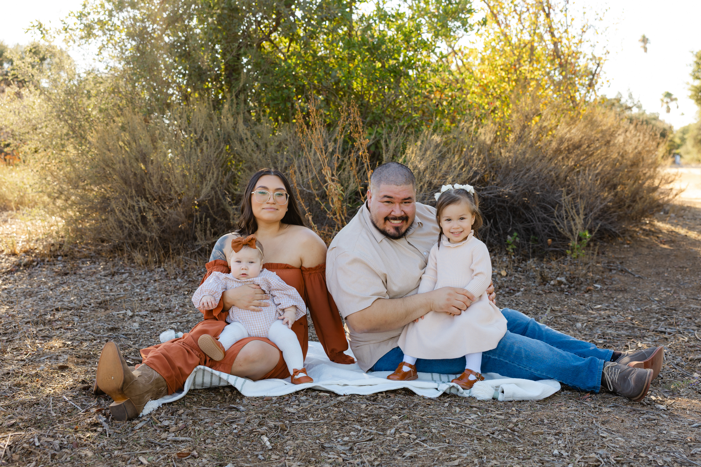 Family sitting together outdoors on a blanket with parents and two young children during a fall family session in the Inland Empire. Photographed by Inland Empire family photographer Kaitlyn Dawn Photography.