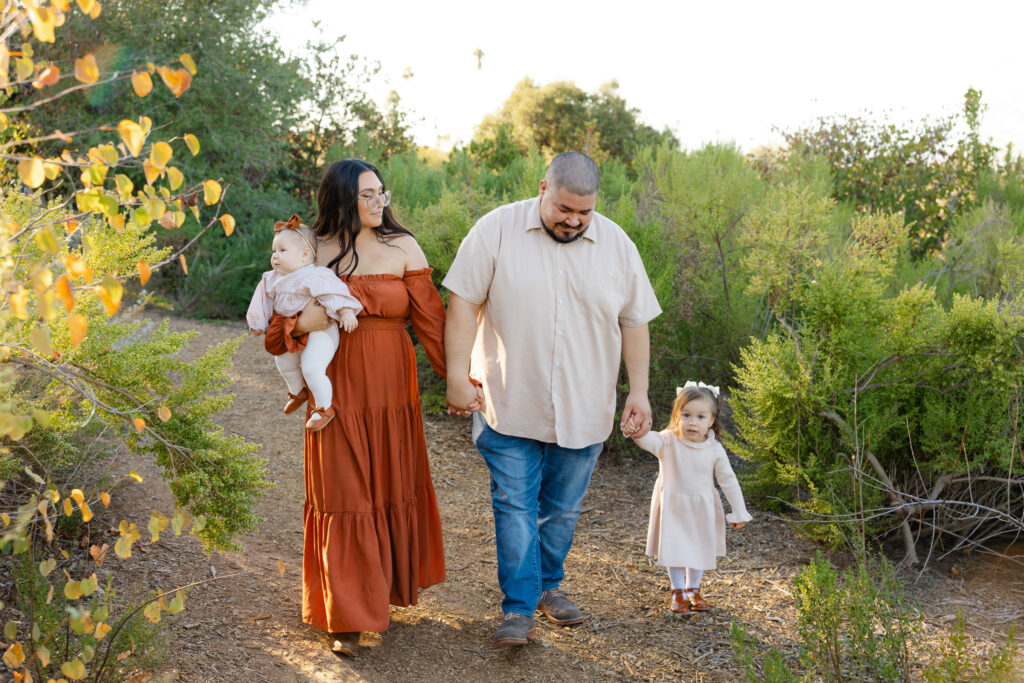 Outdoor family walking together during golden hour with parents holding their daughters, showing why lifestyle family sessions create natural and heartfelt memories.