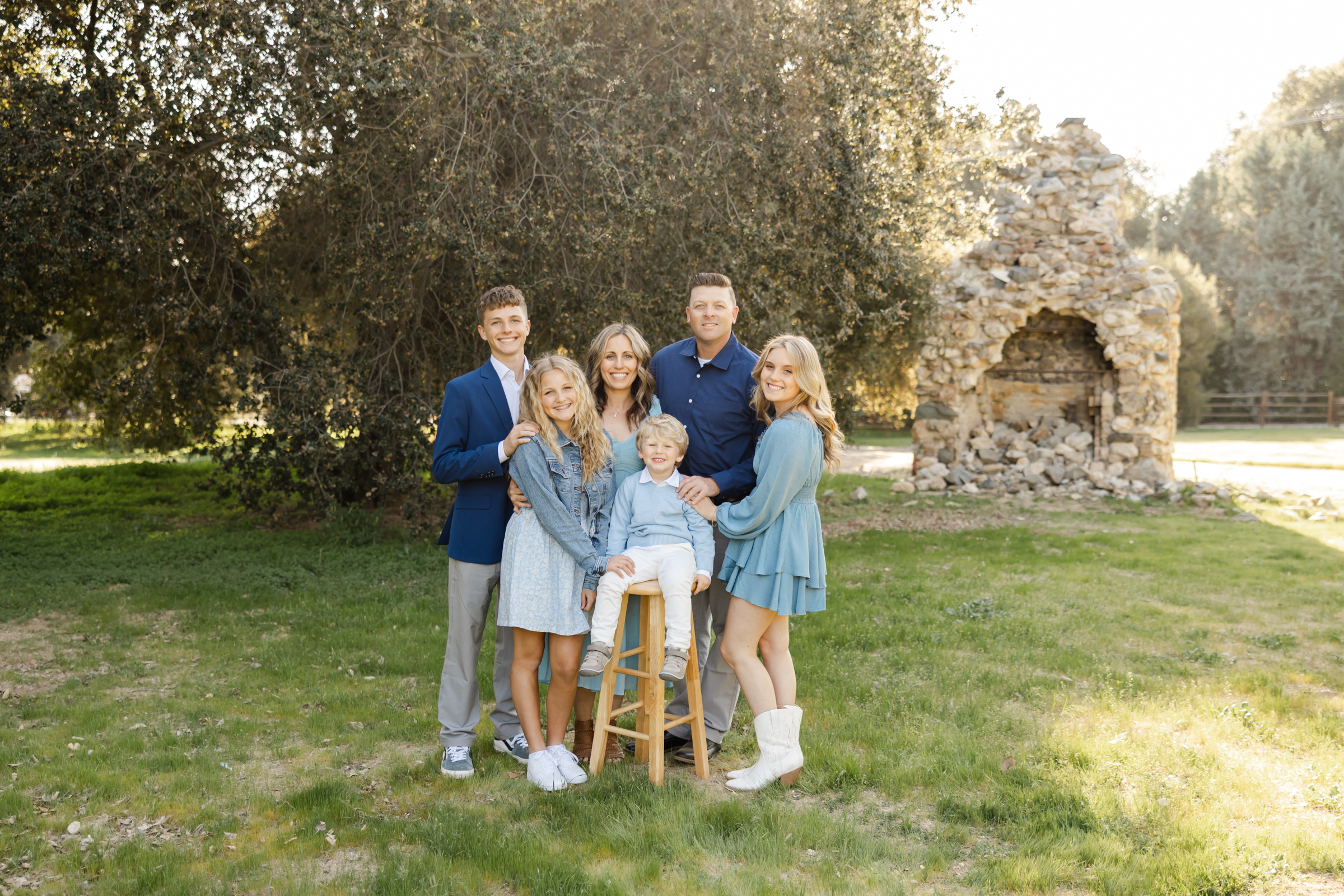 Smiling family portrait outdoors with a stone structure and trees in the background, highlighting things to do in Yucaipa and photographed by Kaitlyn Dawn Photography.