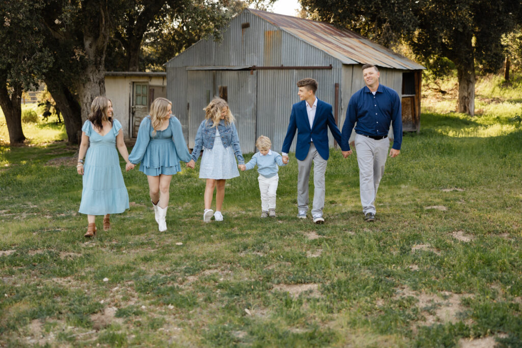 Family walking hand in hand across a grassy field near a rustic barn, enjoying one of the many things to do in Yucaipa, captured by Kaitlyn Dawn Photography.