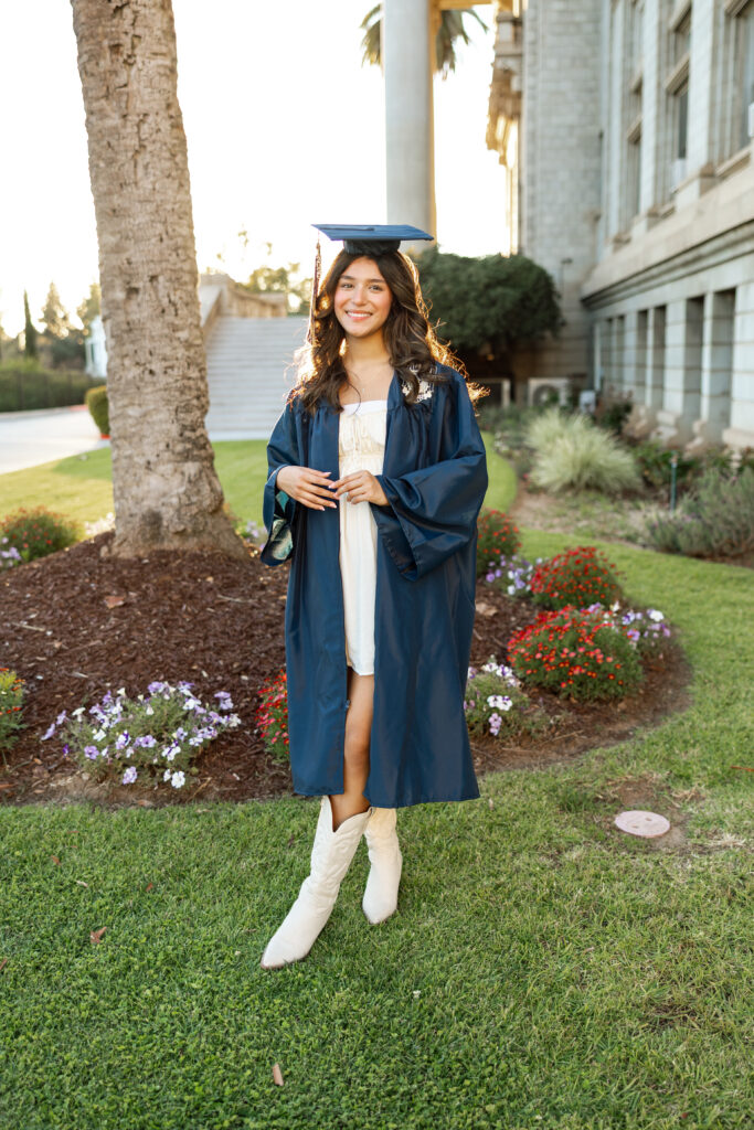 Girl in cap and gown standing on campus lawn at sunset, Inland Empire graduation photos by Kaitlyn Dawn Photography.