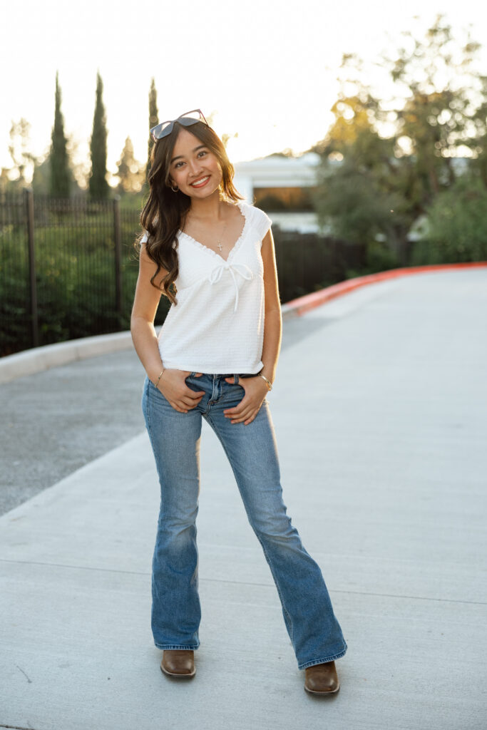 Casual outfit idea for senior pictures featuring a white top, flare jeans, and brown boots in an outdoor setting with Yucaipa senior photographer.