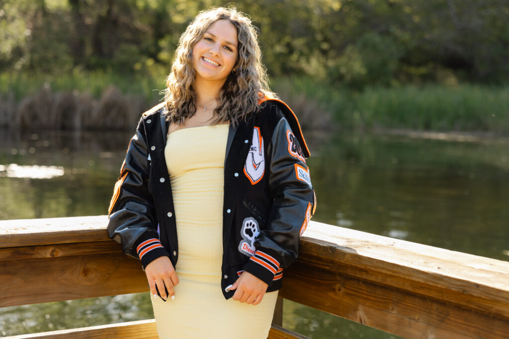 Senior portrait featuring a yellow dress and personalized letterman jacket, an example of mixing personal pieces into senior photos by Kaitlyn Dawn Photographer.