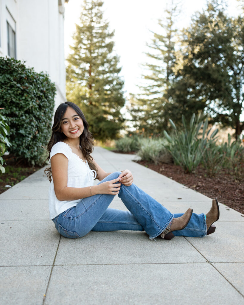 Girl sitting on a sidewalk near greenery in Redlands, captured by Kaitlyn Dawn Photography.