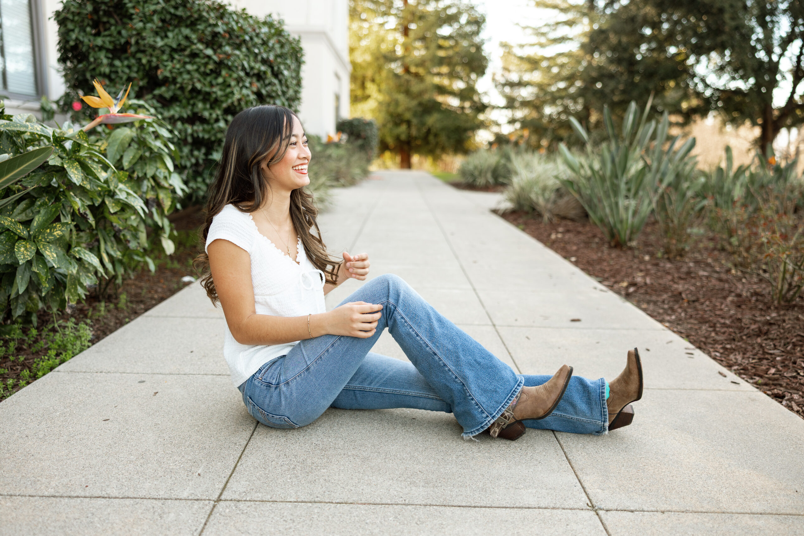 Senior sitting casually on sidewalk in jeans and white top, example of simple outfits when considering what not to wear for senior pictures.