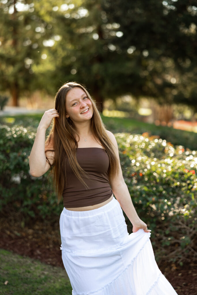 Senior smiling and touching her hair during a relaxed outdoor senior portrait session by a Yucaipa senior photographer.