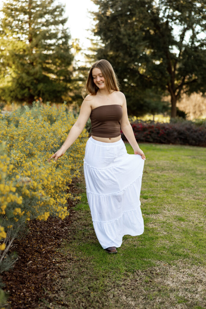 Senior walking through flowers in white skirt in Beaumont, candid senior photo by Kaitlyn Dawn Photography.