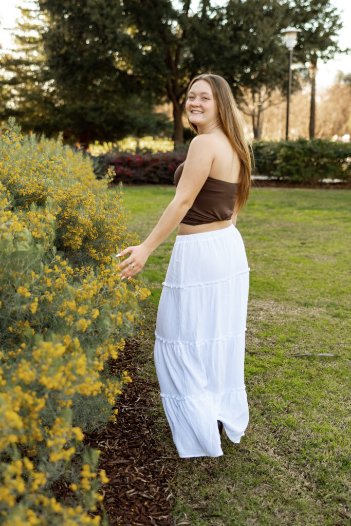 Senior turning toward the camera beside yellow flowers, showing how to not feel awkward in senior photos with guided movement.