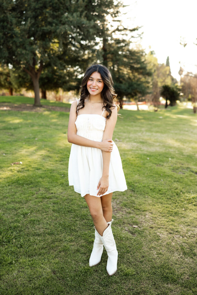 Senior girl in a white dress and boots posing in a sunny park, natural light portrait session in Inland Empire by Kaitlyn Dawn Photography.