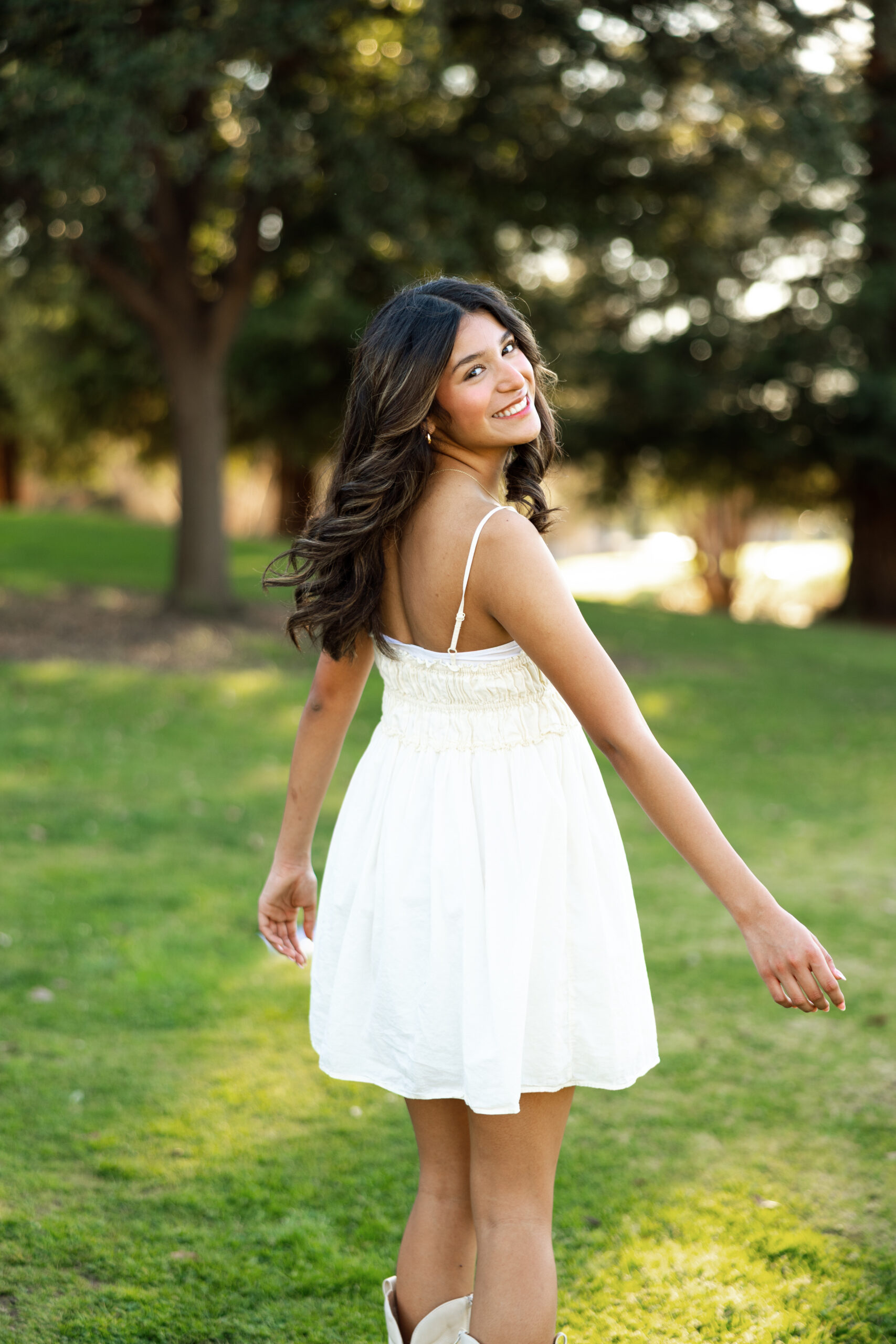 Senior girl twirling and looking back in a white dress in a Redlands park, a great example of natural poses for senior photos.