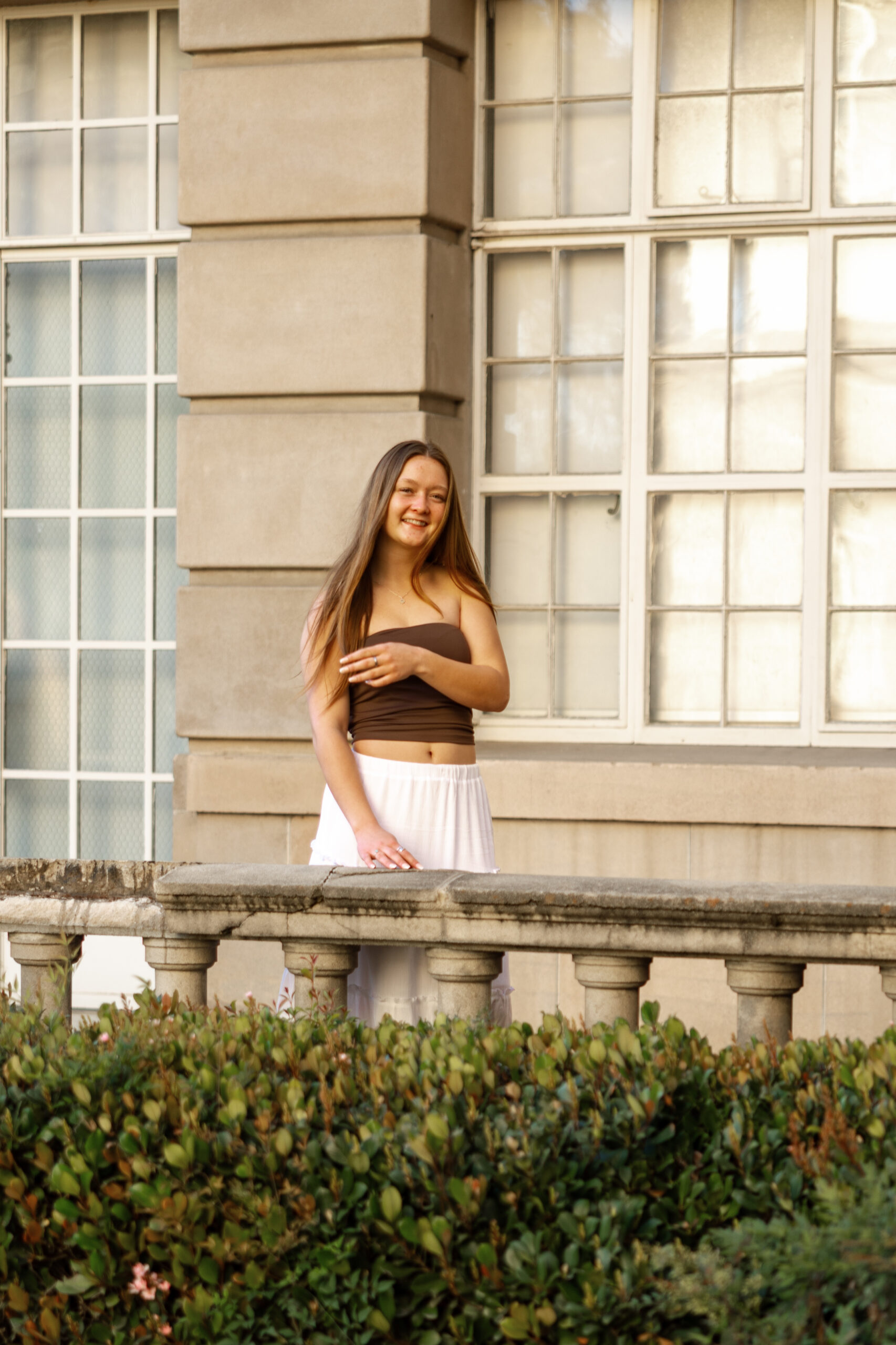 Senior girl in neutral brown and white outfit by building, showcasing best colors for senior photos in soft, warm tones.