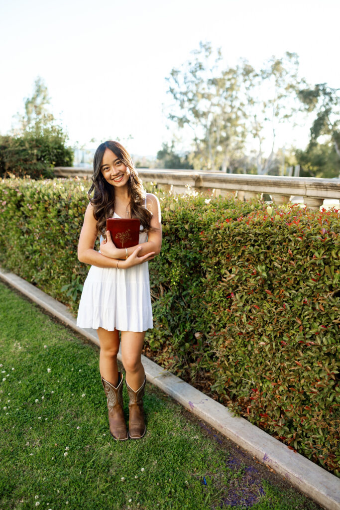 Senior wearing a white dress and cowboy boots outdoors, a personalized outfit idea for senior pictures.