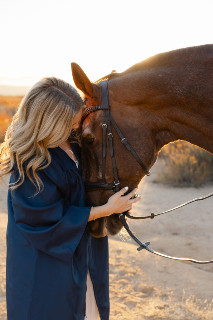 High School girl in graduation gown gently resting her head against her horse, emotional golden hour e by Kaitlyn Dawn Photography.