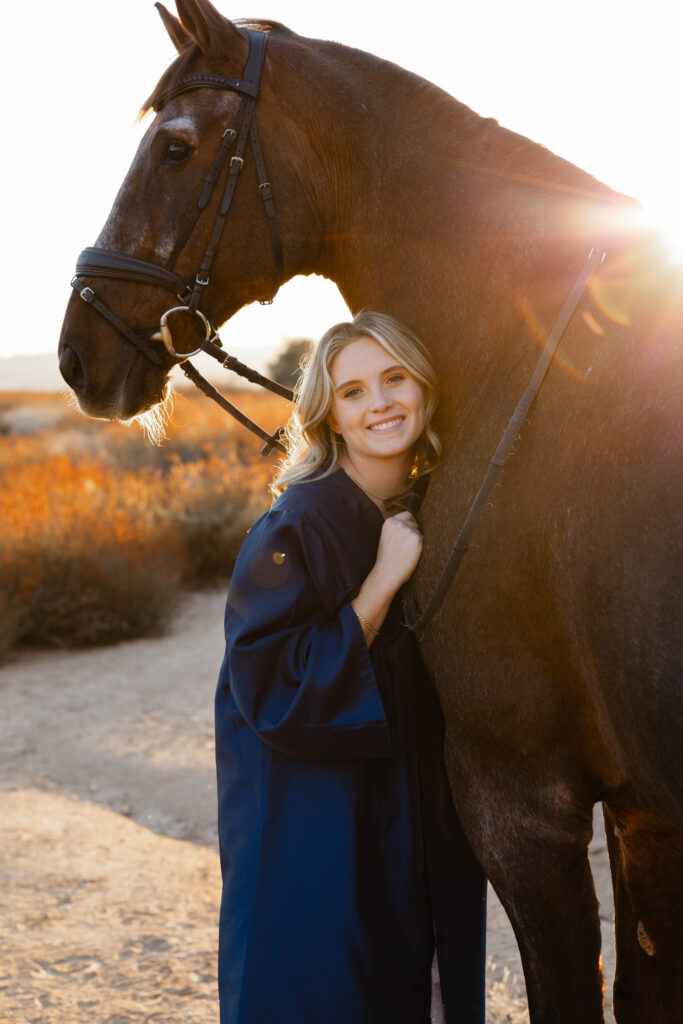 High school girl in cap and gown posing with her horse at sunset, warm golden hour Redlands senior portrait story.