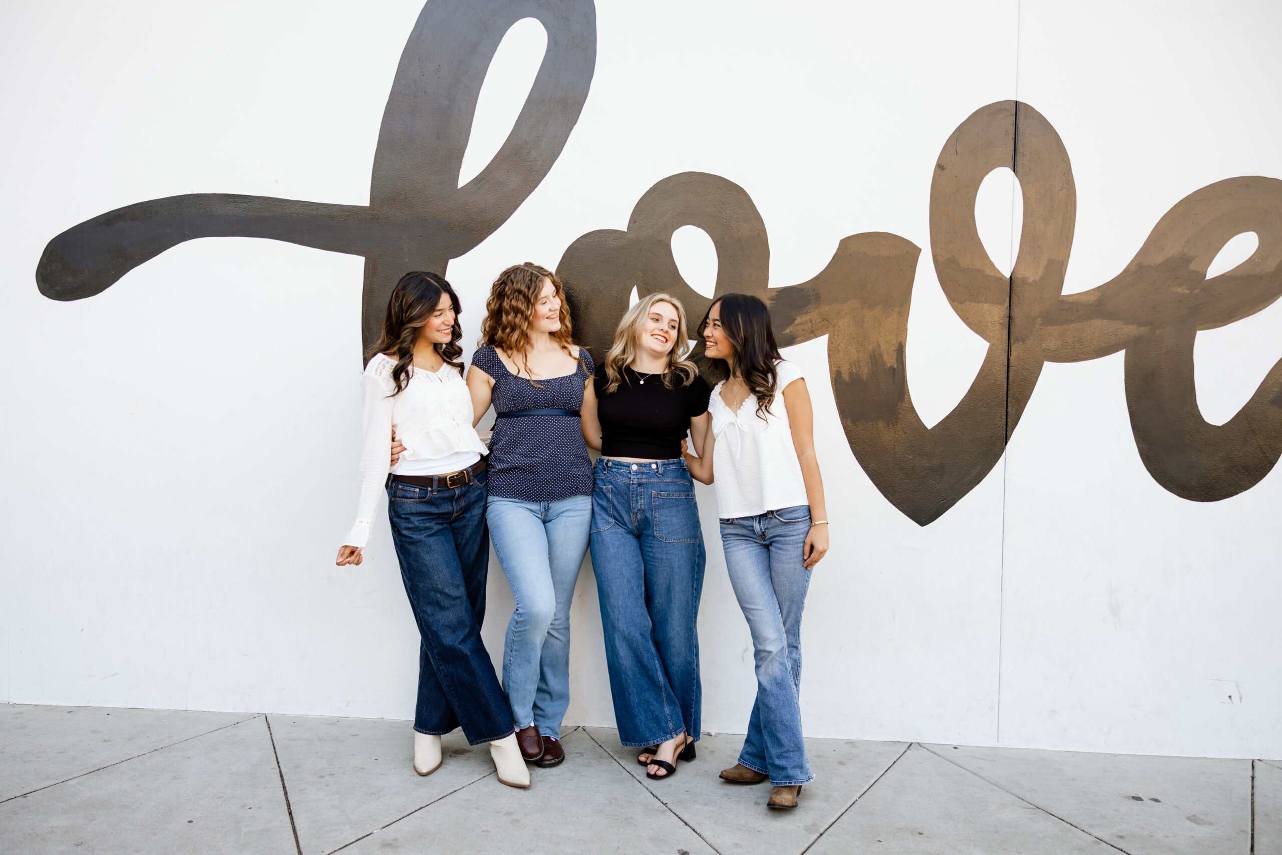 Four high school seniors standing together in Redlands, smiling in casual denim outfits during a session that shows how to prepare your senior session with friends.