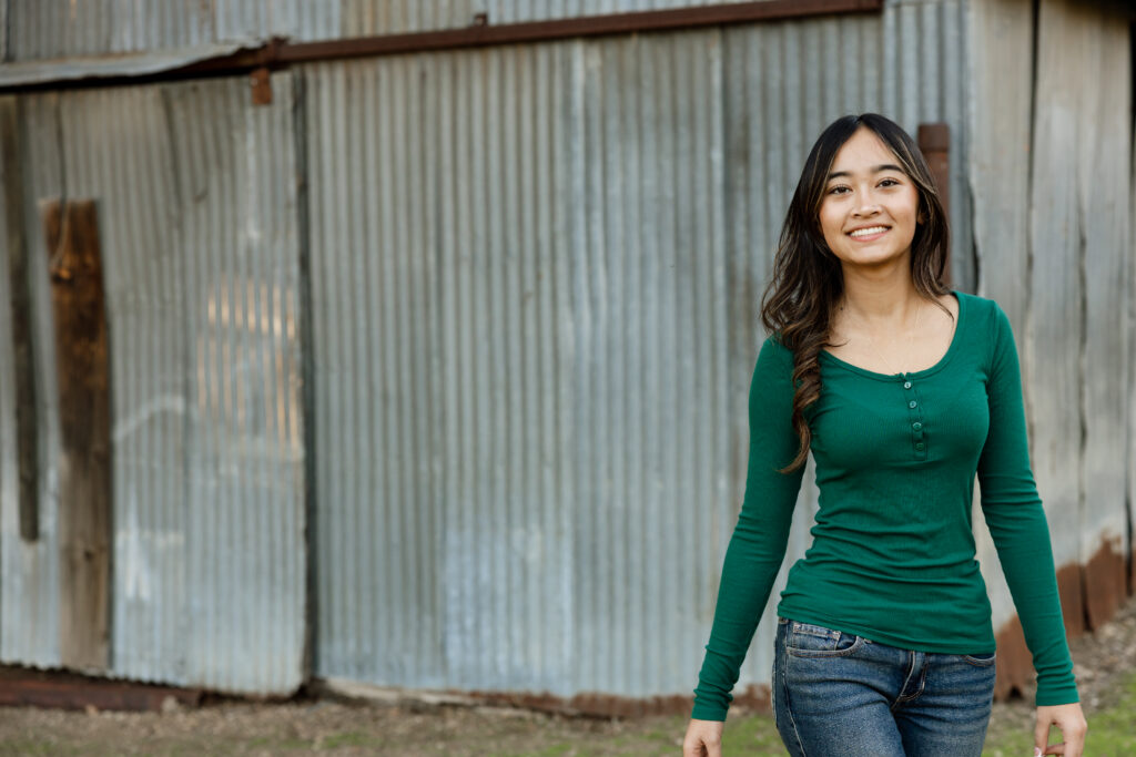 Senior girl walking near a rustic metal building in a casual outfit, natural movement example of how to pose for senior photos in Inland Empire by Kaitlyn Dawn Photography.