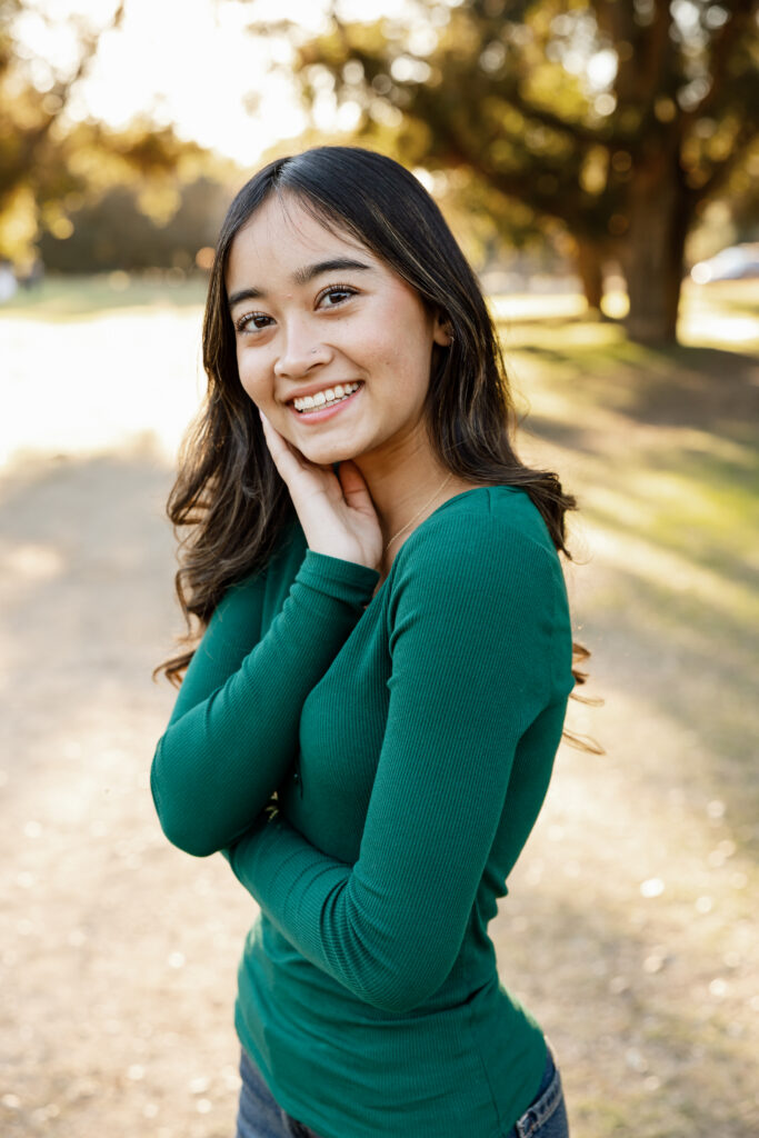 Senior portrait of girl in green top smiling in a sunlit park in Redlands, highlighting indoor vs outdoor senior photos by Kaitlyn Dawn Photography.