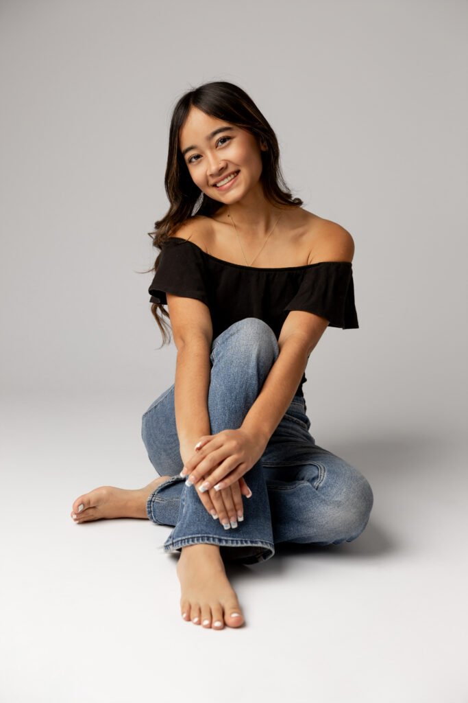Girl seated cross-legged in studio with neutral backdrop in Redlands, by Kaitlyn Dawn Photography.