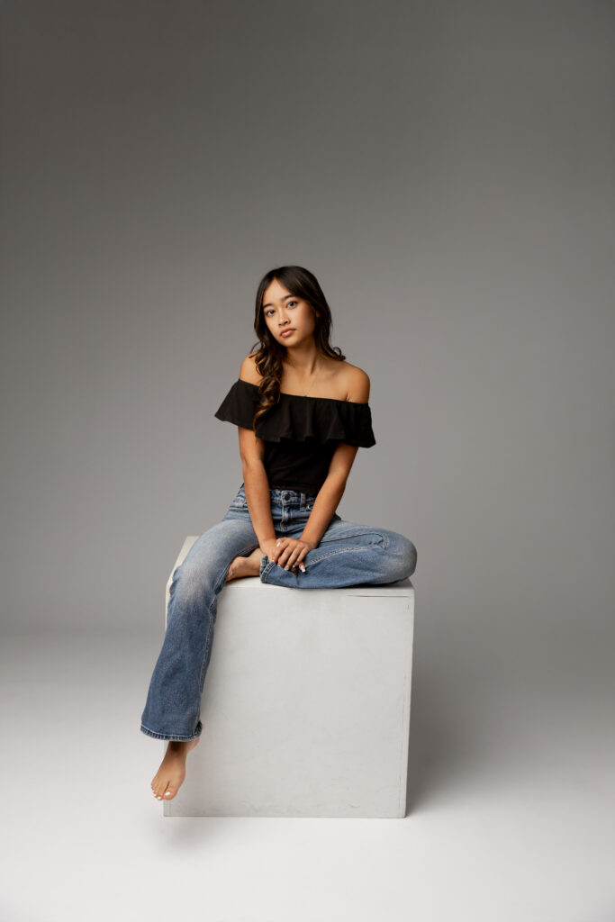 Senior girl sitting on a white cube in studio setting in Redlands, showcasing indoor vs outdoor senior photos by Kaitlyn Dawn Photography.