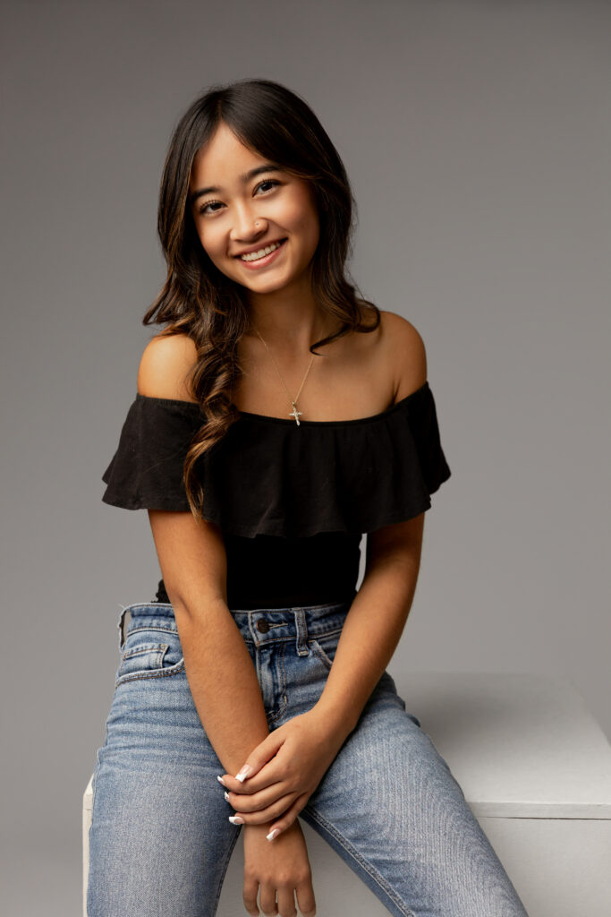 Studio senior portrait of girl in black top and jeans against neutral backdrop, representing indoor vs outdoor senior photos in Redlands by Kaitlyn Dawn Photography.