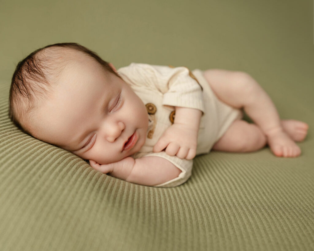 Sleeping baby posed on a sage green blanket during a 6 week newborn milestone session, capturing the peaceful expressions and growing personality of early infancy.