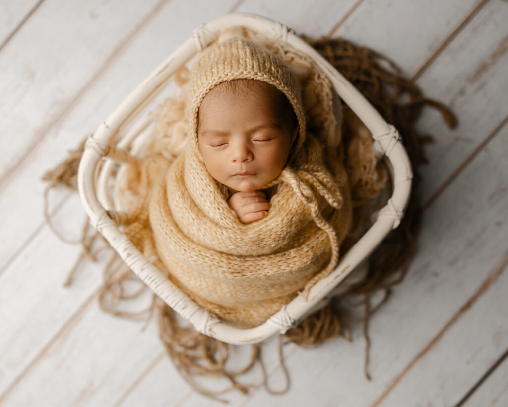 Overhead portrait of a swaddled infant resting in a basket during newborn week 3, capturing the tiny details and sleepy expressions that change so quickly.