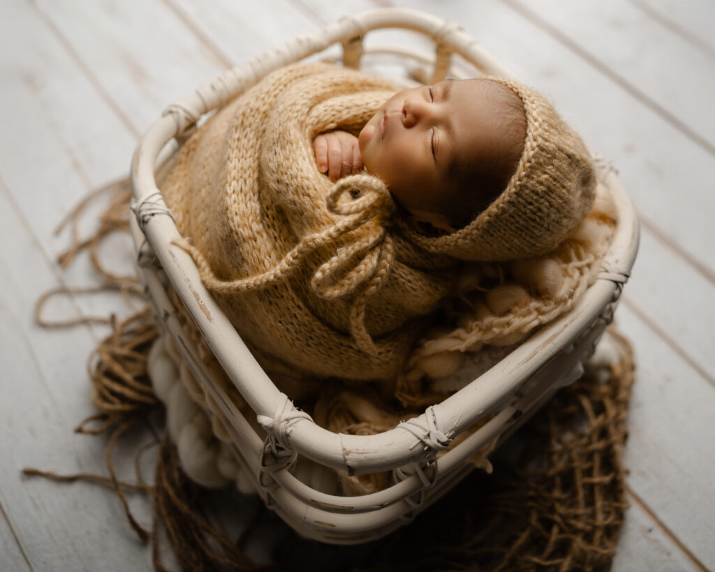 Newborn week 3 baby curled comfortably in a woven basket with neutral-toned wraps, photographed by a Yucaipa newborn photographer during a baby-led session.