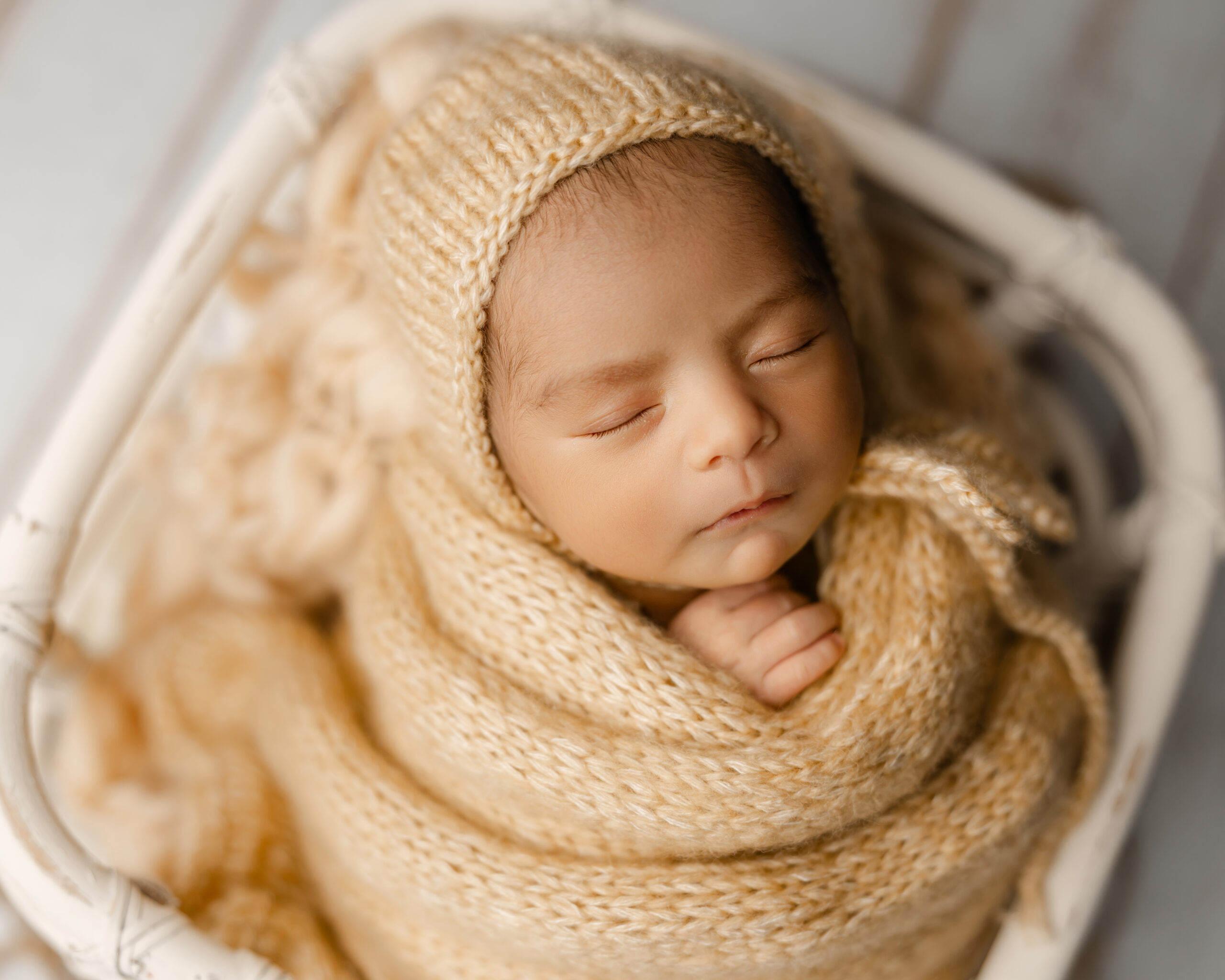 Close-up portrait of a sleeping newborn week 3 baby wrapped in soft knit layers, highlighting the delicate features often photographed during the first month of life.